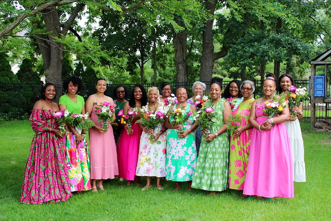 Iota Zeta Omega sorors in pink and green dresses holding bouquets of flowers in a garden
