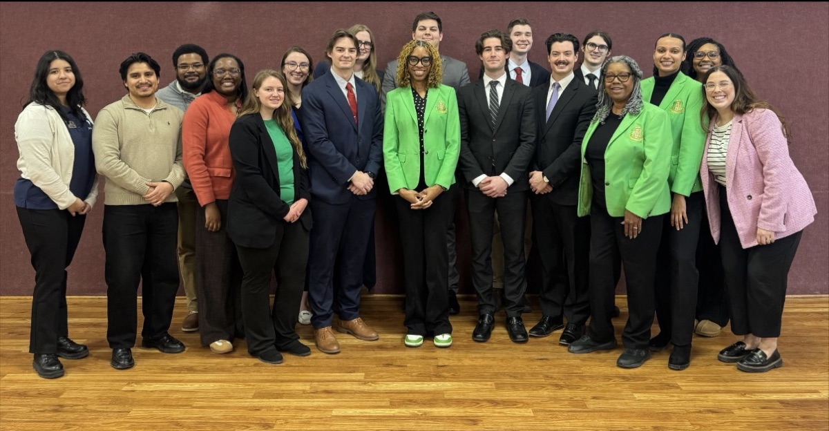 Iota Zeta Omega members in green blazers with a group of students and community members