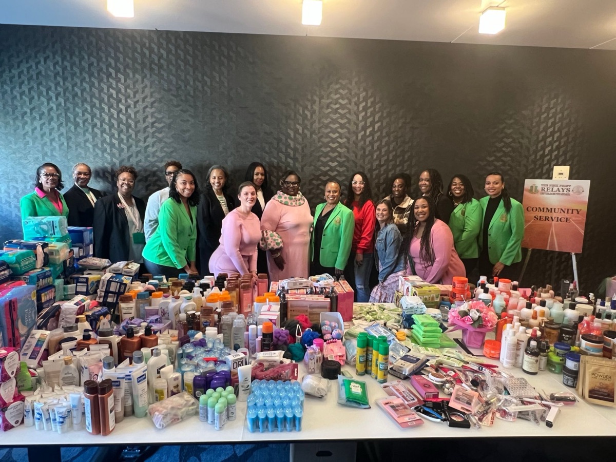 Sorors with tables of donated toiletries and personal care items at a Pink Print Relays community service project