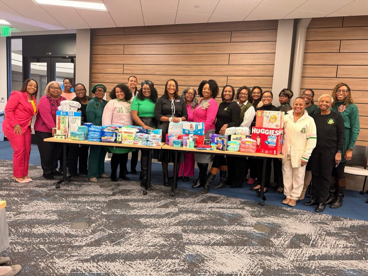 Iota Zeta Omega members with tables of donated diapers, wipes, and baby supplies
