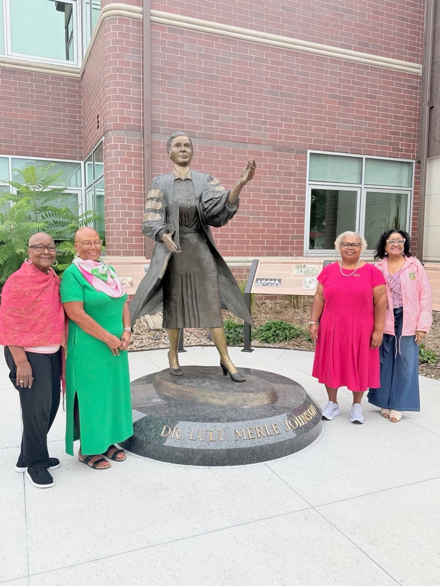 Four Iota Zeta Omega members beside the statue of Dr. Lulu Merle Johnson