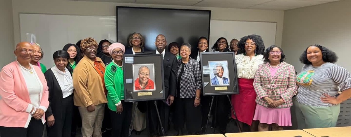 Iota Zeta Omega members and guests with two framed portraits at a portrait unveiling