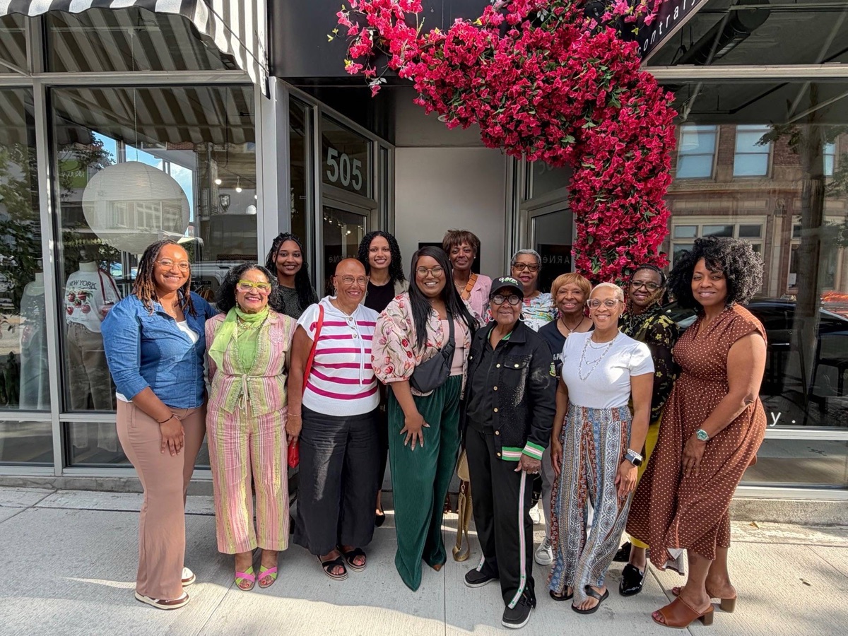 Sorors outside a storefront under an arch of pink flowers